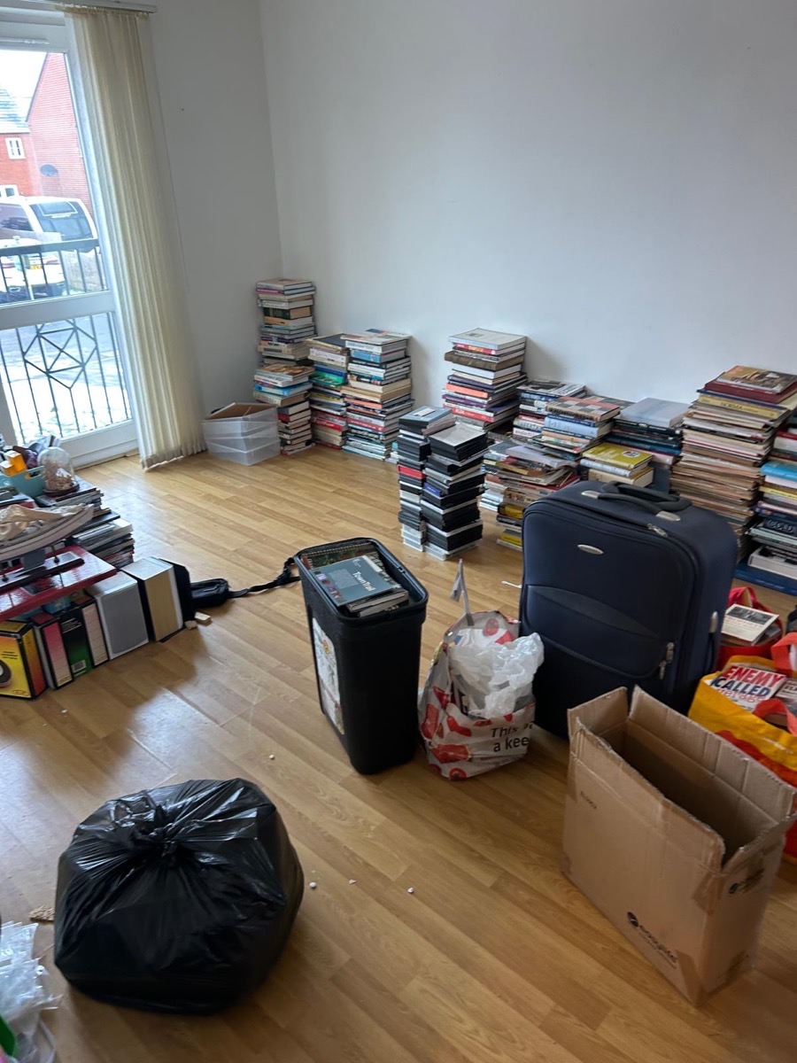 Flat living room stacked with books, boxes and a suitcase before clearance