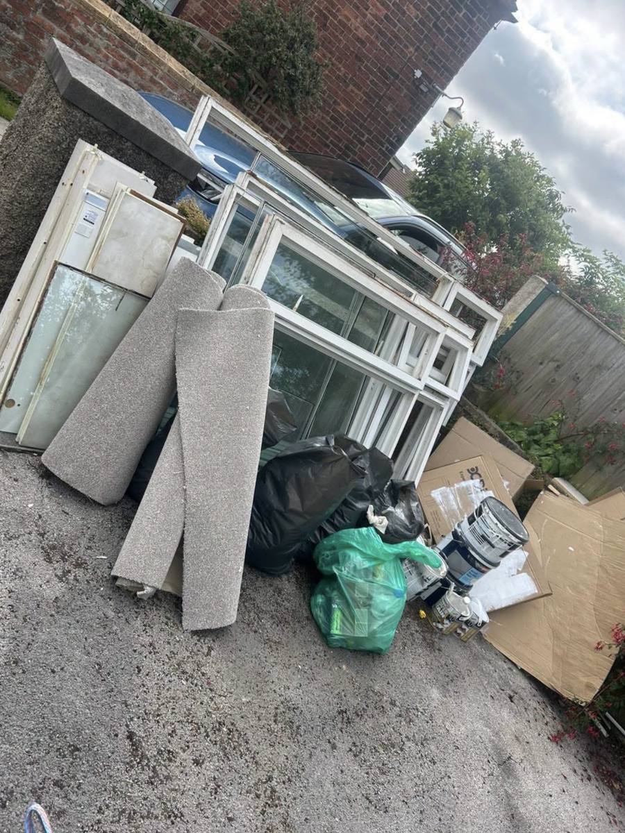 Yard corner piled with old windows, carpet and cardboard before clearance