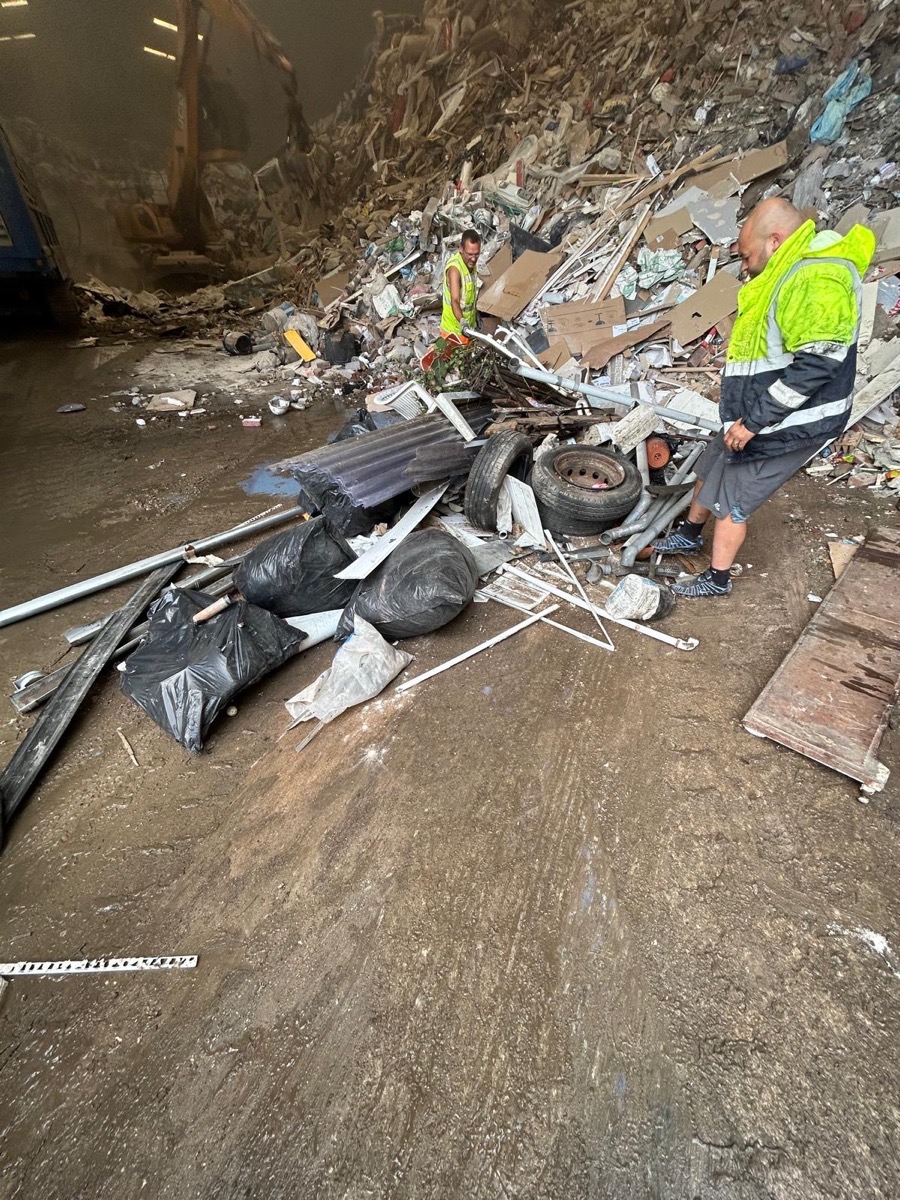 Staff sorting waste at a licensed transfer facility, with a JCB loader in the background
